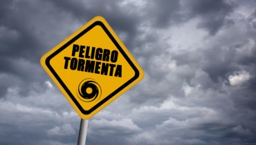 Señal amarilla de desastres naturales al fondo de un cielo nublado que dice PELIGRO TORMENTA