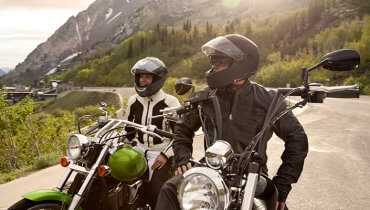 Pareja joven de viaje sobre sus motocicletas contemplando el paisaje usando un casco de moto