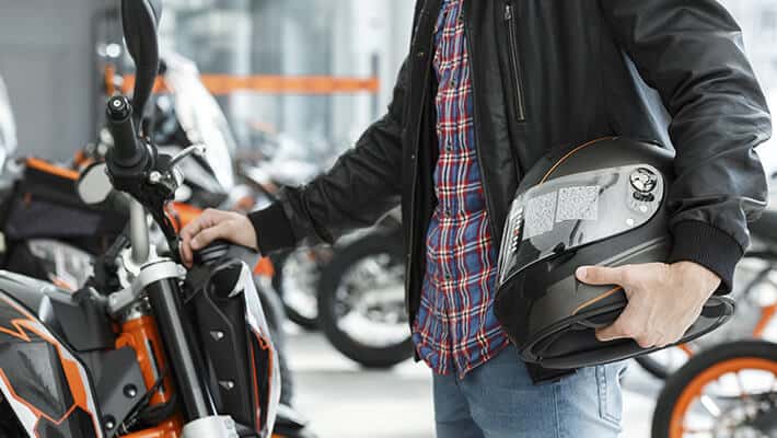 Hombre sosteniendo un casco de moto con una mano frente a su motocicleta