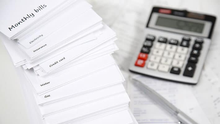 Pila de papeles con nombres en inglés de gastos mensuales junto con una calculadora