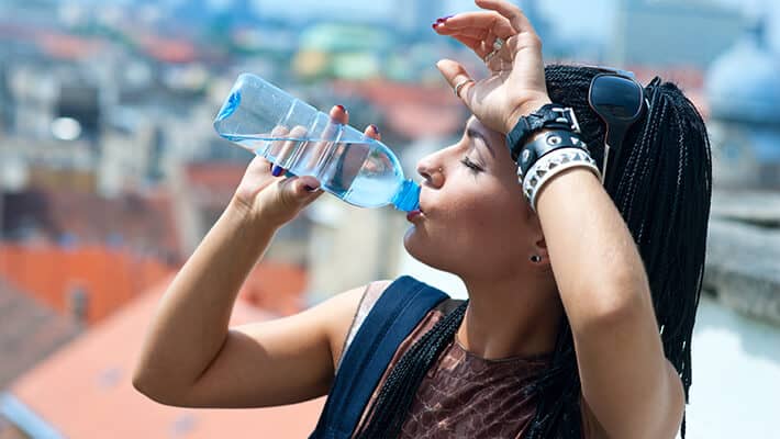 Mujer bebiendo agua de botella al aire libre para cuidarse de los climas extremadamente cálidos