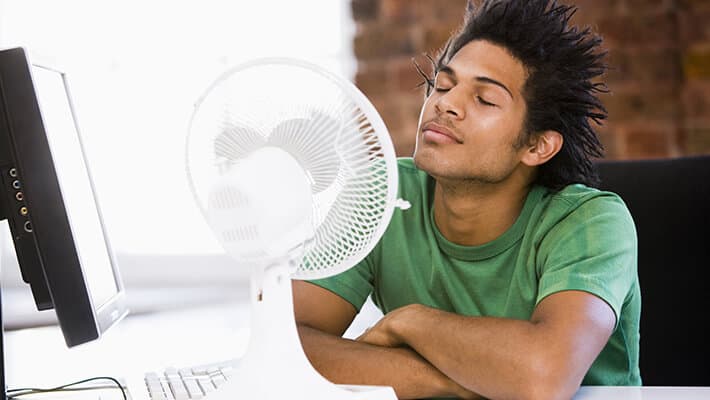 Hombre fente de un ventilador de mesa para cuidarse en los climas extremadamente cálidos