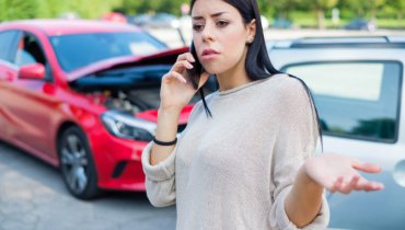 Mujer con auto chocado hablando por telefono móvil sobre que hacer con un conductor sin seguro