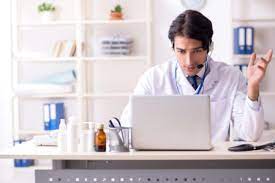 Médico joven con diadema frente a su laptop haciendo telemedicina en un consultorio