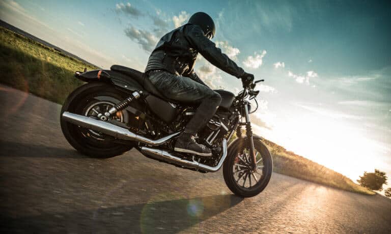 Hombre de chaqueta de cuero conduciendo en la carretera su motocicleta negra con el cielo despejado