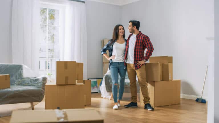 Pareja joven abrazados sonriendo rodeados de cajas y muebles en un apartamento nuevo