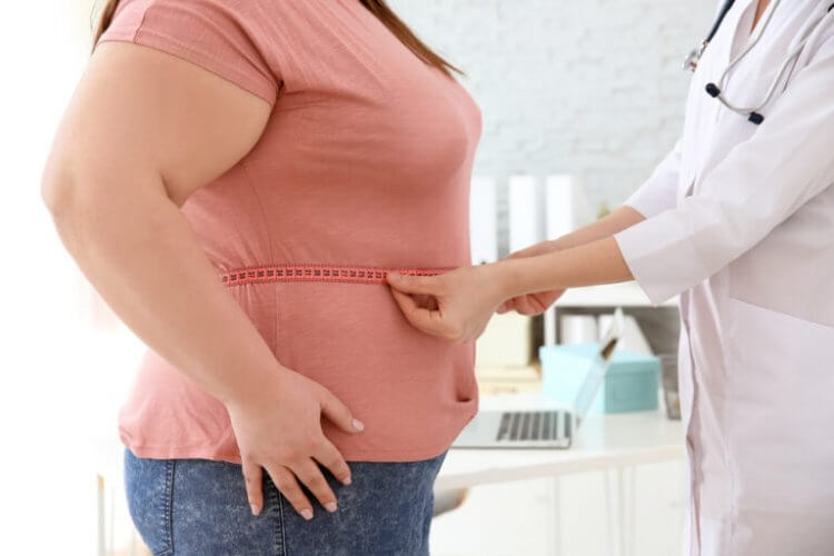 Doctora midiendo con un metro la cintura de una paciente obesa para su seguro médico