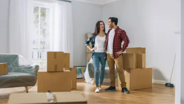 Pareja joven abrazados sonriendo rodeados de cajas y muebles en un apartamento nuevo