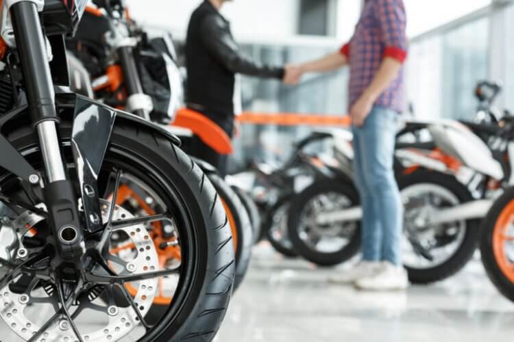 Hombre joven saludando a un asesor en una tienda para comprar una moto usada