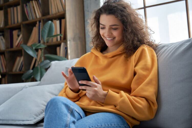 Mujer sonriendo revisando su smartphone sentada en el sofá para encontrar seguro médico