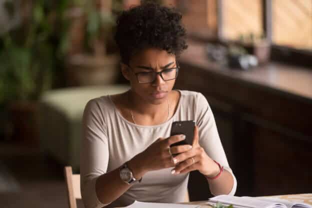 Mujer sentada en su escritorio mirando su smartphone pensando que pasa cuando te roban la identidad