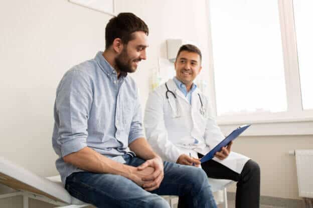 Doctor sonriente sentado revisando el seguro médico y la inscripción abierta con su paciente