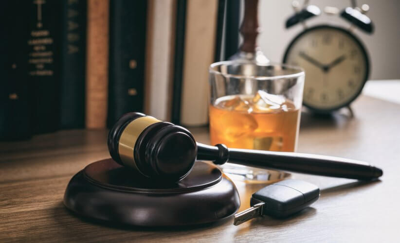 Mazo de juez indicando un caso de DUI con una llave y vaso de licor en escritorio