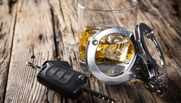 Llaves de auto y esposas métalicas sobre un vaso de licor de quien cometió un DUI en California