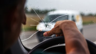 Hombre frente al volante arriesgandose a conducir con el parabrisas roto sin seguro