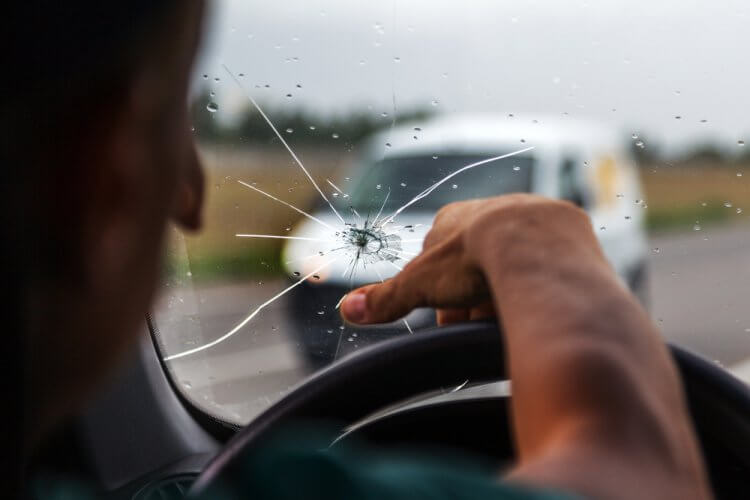 Hombre frente al volante arriesgandose a conducir con el parabrisas roto sin seguro