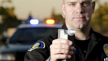 Policía rudo sosteniendo un alcoholímetro diciendo las consecuencias de un DUI en California