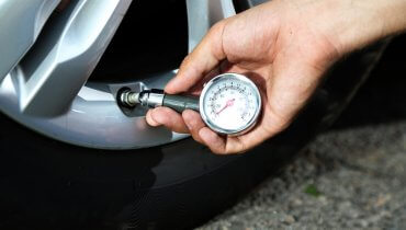 Hombre usando un medidor de velocidad para medir la presión de las llantas de su auto
