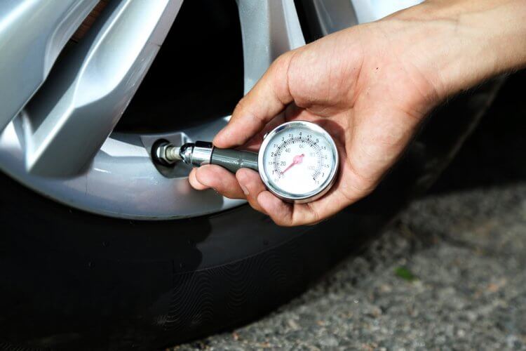 Hombre usando un medidor de velocidad para medir la presión de las llantas de su auto