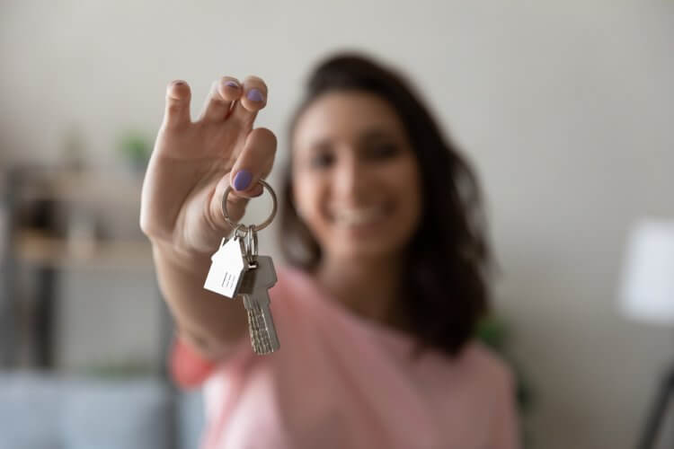 Mujer joven sonriendo y sosteniendo de las manos sus nuevas llaves al rentar casa