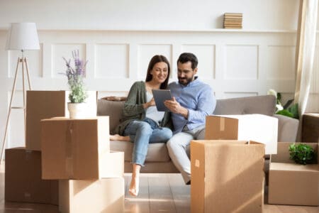 pareja feliz sentada en su nuevo departamento de renta viendo una tablet