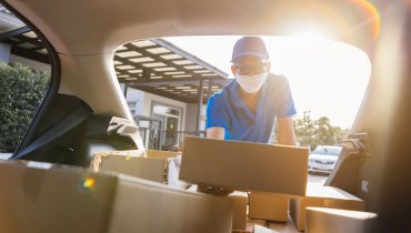 Hombre distribuidor de amazon con mascarilla depositando varias cajas dentro de su auto