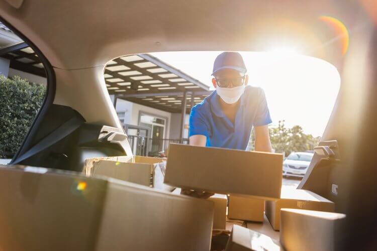 Hombre distribuidor de amazon con mascarilla depositando varias cajas dentro de su auto