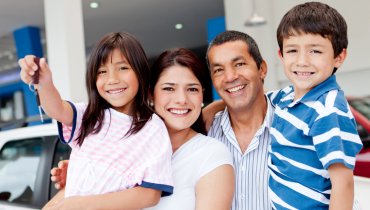 Familia feliz que acaba de comprar un auto usado y muestra las llaves en el concesionario