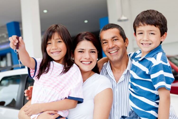 Familia feliz que acaba de comprar un auto usado y muestra las llaves en el concesionario