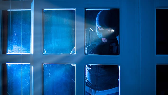 Ladrón observando detrás de una puerta de vidrio con una linterna para robar