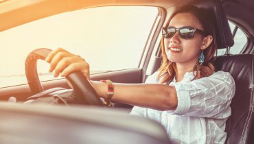 Mujer joven con gafas oscuras al volante conduciendo un auto con seguro nuevo
