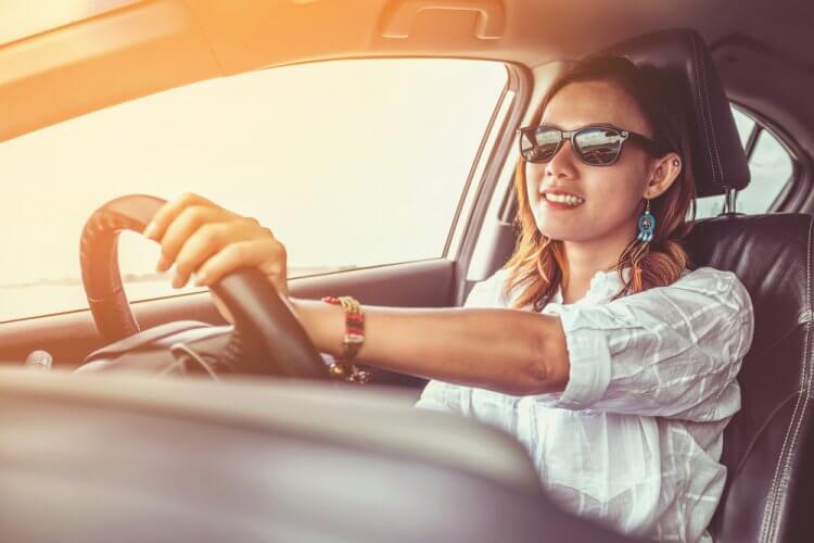 Mujer joven con gafas oscuras al volante conduciendo un auto con seguro nuevo