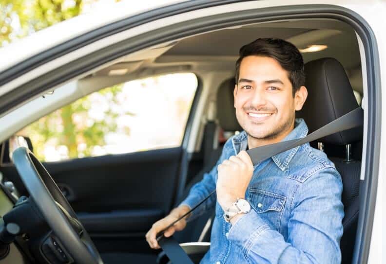 Hombre joven sonriendo dentro de un auto colocando su cinturon de seguridad