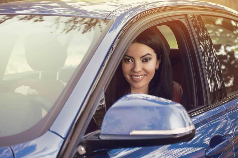mujer hispana sonriente conduciendo auto azul con seguro y deducible