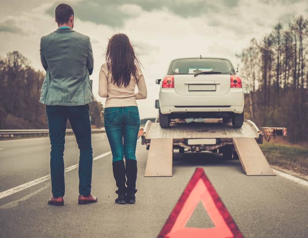 hombre y mujer a un lado de un auto en una grúa en carretera