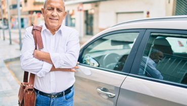 hombre latino mayor sonriendo frente a su auto con seguro basico