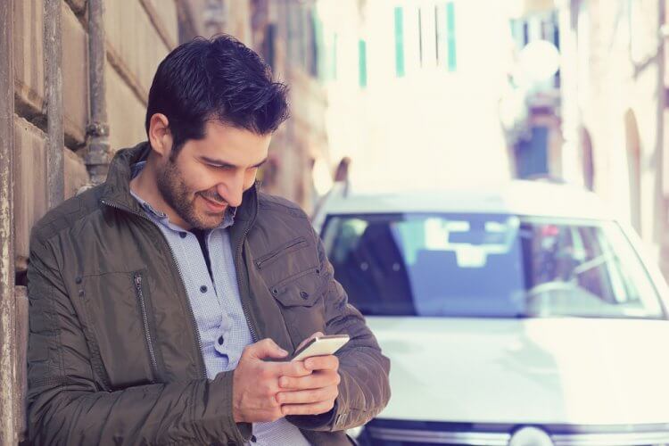 hombre sonriente viendo telefono movil con auto de fondo