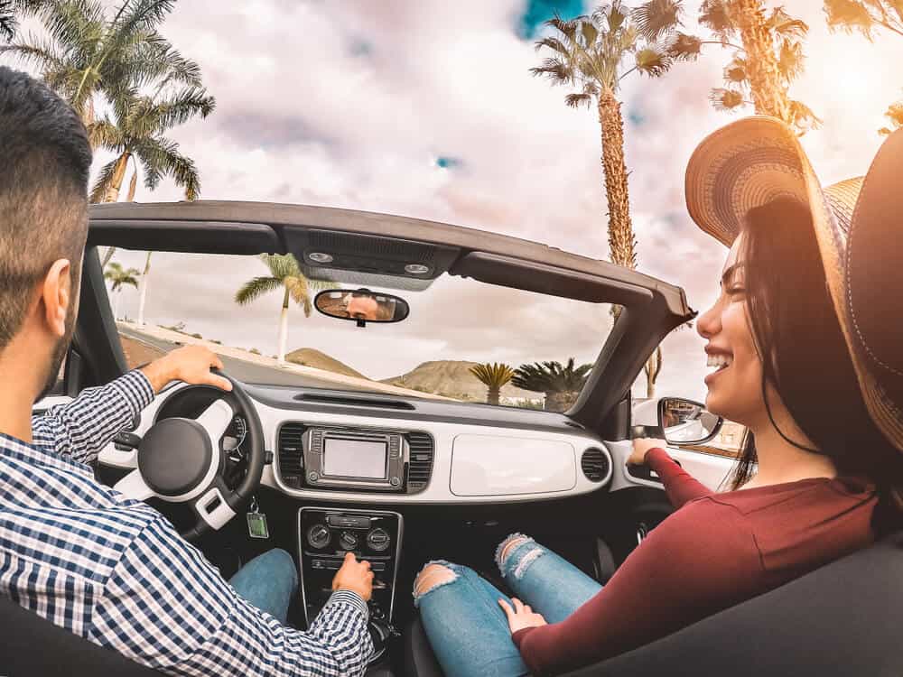 pareja hispana feliz manejando un auto convertible con seguro
