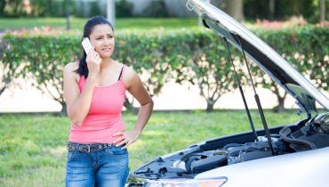 mujer joven a un lado de auto averiado hablando por celular