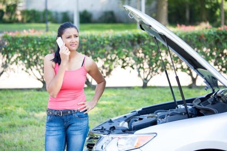 mujer joven a un lado de auto averiado hablando por celular