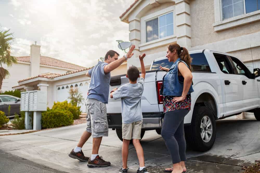 happy family highfiving with a pickup truck and home in the background