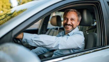 hombre mayor latino sonriente conduciendo su auto con seguro