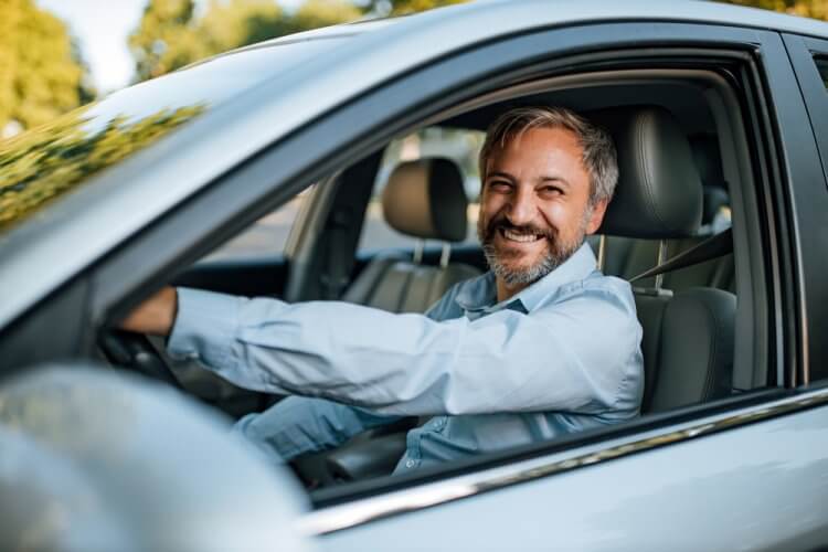 hombre mayor latino sonriente conduciendo su auto con seguro