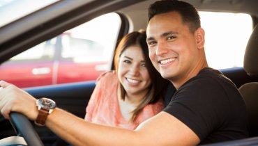 pareja hispana feliz en auto viendo a la camara