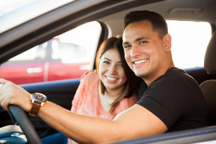 pareja hispana feliz en auto viendo a la camara
