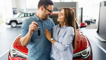 pareja feliz frente a su auto nuevo y el hombre está sosteniendo las llaves