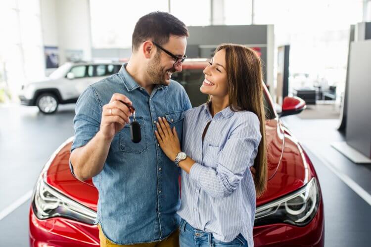 pareja feliz frente a su auto nuevo y el hombre está sosteniendo las llaves