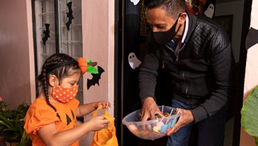 hombre hispano con cubreboca repartiendo dulces en halloween a niña