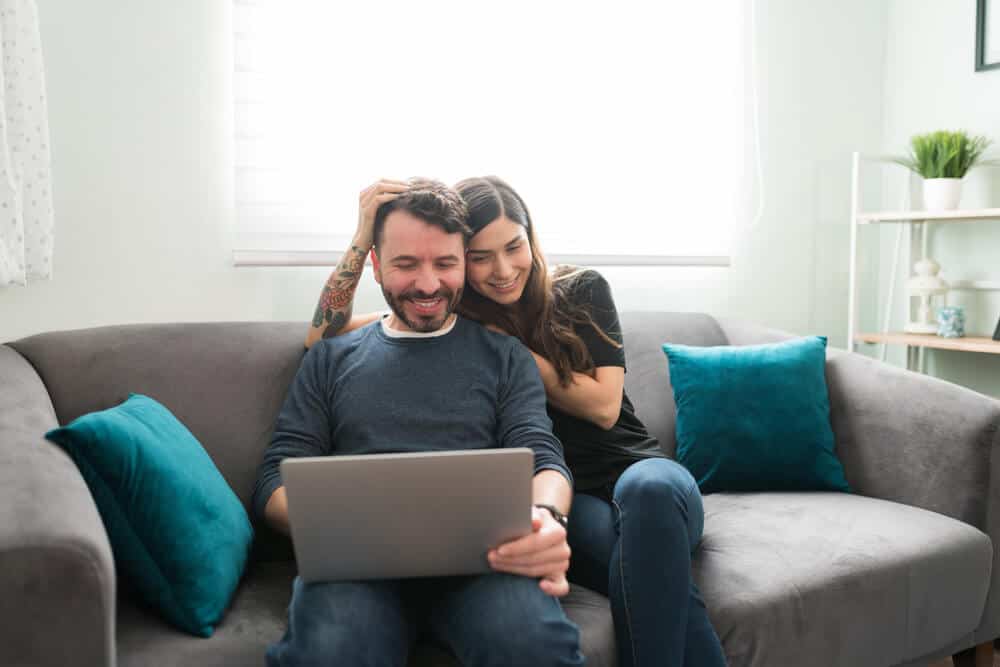 Dos jóvenes sentados en un sillón frente a una computadora portátil