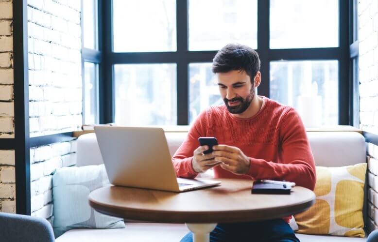 Hombre hispano viendo su telefono movil y computadora portatil en una cafeteria